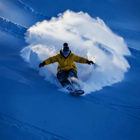 a snowboarder carving through powder, leaving behind an arc of white on the pristine surface of deep blue snow. award-winning photography, in the style of realistic photography. 