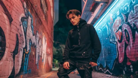 (masterpiece, best quality, cinematic lighting, absurdres), 1boy, handsome young man, short black hair, serious expression, wearing a black hoodie and cargo pants, leaning against a graffiti wall on a city street at night, neon lights, rim light, detailed clothing texture, dynamic angle, full body shot
