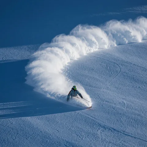 a snowboarder carving through powder, leaving behind an arc of white on the pristine surface of deep blue snow. award-winning photography, in the style of realistic photography. 
