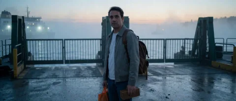 A cinematic coastal mystery still of a foreign adult man waiting at an empty ferry terminal before sunrise, holding a small wooden box, fog covering the water, distant ferry lights barely visible, cold blue atmosphere, expression of hesitation and hope, realistic movie photography, wide composition, ultra-detailed