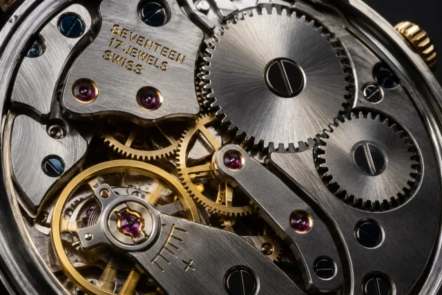 Extreme macro photograph of an open mechanical wristwatch movement, intricate gears and jewels, brushed steel and gold plating, dramatic studio lighting, ultra-detailed